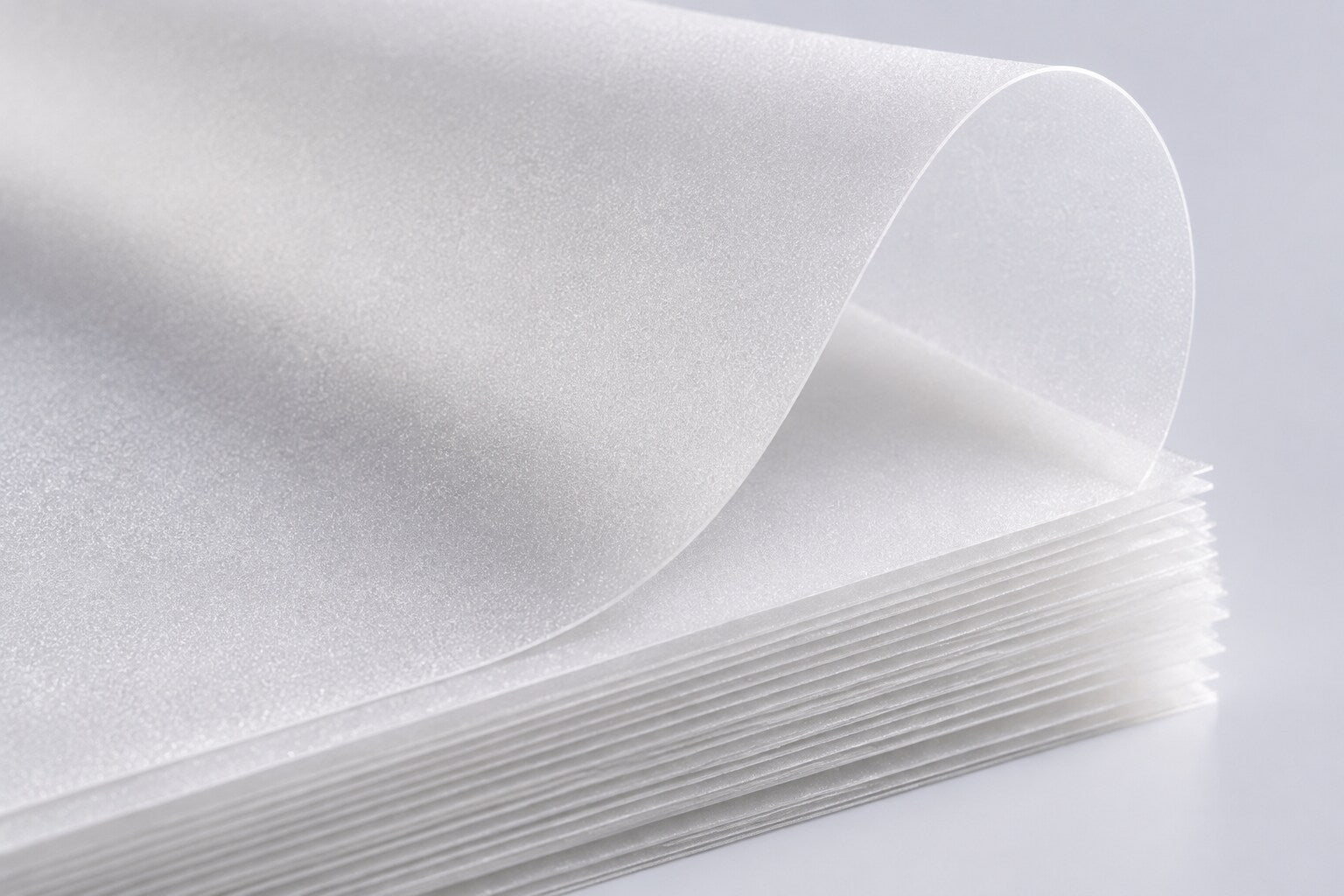 Close-up of frosted white polypropylene sheets showing distinct fine granular texture, stacked edges and a flexible curled top sheet